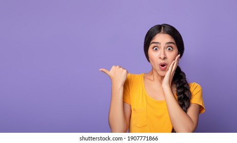 Omg, Cool Offer. Surprised young indian lady pointing at free space isolated over purple studio background. Excited shocked woman showing copy space and place for advert or promotional text, banner