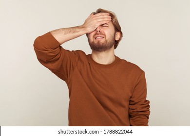 Omg, facepalm! Portrait of desperate man keeping hand on head blaming himself for bad memory, unforgivable mistake, expressing sorrow and shame emotion. indoor studio shot isolated on gray background