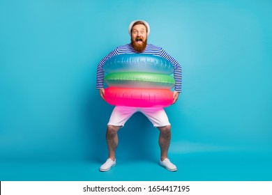 Omg ocean. Full body photo of cheerful excited man enjoy summer tourism vacation hold three float rings want swim wear white sunhat shorts isolated over blue color background