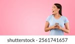 Omg. Portrait of excited shocked female model holding and using smartphone, standing isolated over yellow studio background, looking away at free copy space with open mouth, banner, panorama