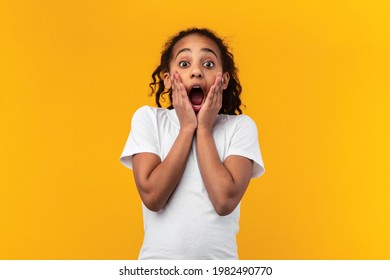 Omg. Portrait of excited surprised black girl touching her face and cheeks, looking at camera with open mouth, shocked by great offer, standing isolated over yellow orange studio background - Powered by Shutterstock