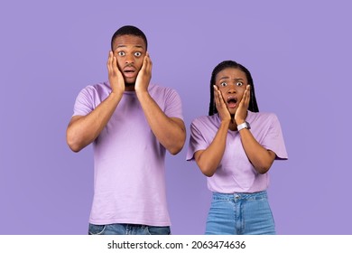 Omg. Portrait of scared African American couple touching face and cheeks, shocked woman and man looking at camera standing isolated on purple violet studio background. Human emotion, facial expression