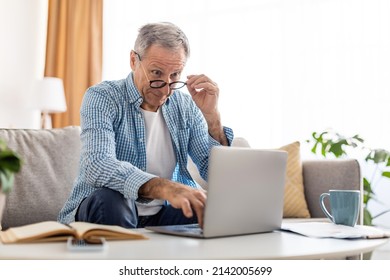 Omg, Wow. Portrait Of Surprised Mature Man Sitting At Desk On Couch Using Laptop, Taking Off Glasses Looking At Pc Screen In Amazement. Emotional Male Reading Breaking News Online In Home Office