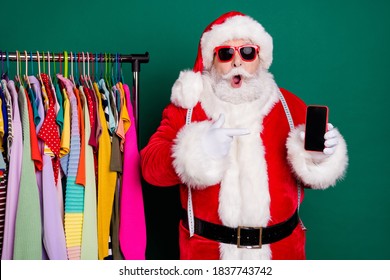 Omg x-mas eve noel gadget discount. Amazed santa claus shopper buyer boutique showroom designer point finger smartphone impressed wear red cap headwear isolated green color background - Powered by Shutterstock