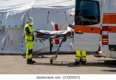 Omicron 5 Alert. Paramedics With Protective Masks Prepare To Assist A Sick Person With Corona Virus Inside An Ambulance. Setting Up A Stretcher Near An Emergency Hospital Field Tent For The First AID	