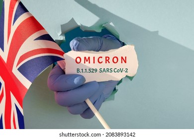 Omicron in United Kingdom, new corona virus variant of concern in Great Britain, UK. Hand in glove from torn paper hole holds british flag and scrap of paper with name of the new coronavirus variant.