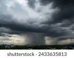 Ominous dark clouds release a heavy downpour over a cityscape, signaling a sudden rainstorm.