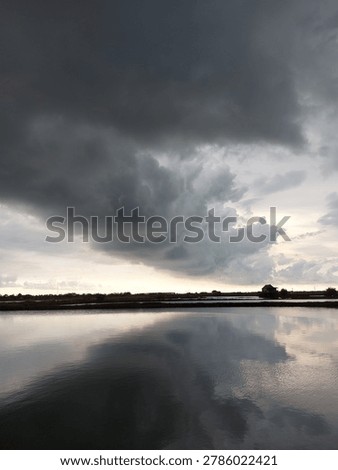 Ominous storm clouds and rainclouds before rain reflected on calm water surface at dusk, dramatic weather sky with copy space.