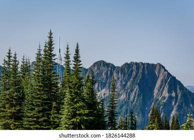 Omni Communications Antenna On A Small Tower Camouflaged In Evergreen Trees, Mountain Ridge And Sky In Background
