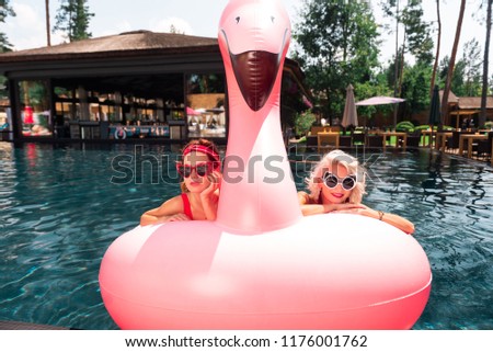 On an air flamingo. Nice happy women being in the middle of the pool while swimming on an air flamingo