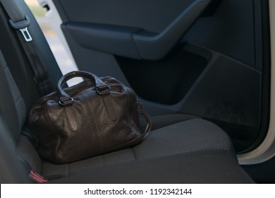 On The Back Seat Of The Car Is A Brown Leather Bag On The Background Of The Door Ajar. Forgotten.