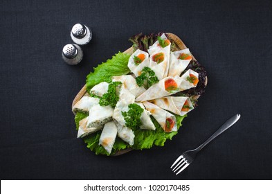 on the background of dark fabric pita roll with salmon and Philadelphia cheese, beautifully laid out, next fork and Solyanka, with salt and pepper