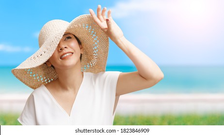 On the beach Portrait of beautiful young asian woman wearing straw hat wide brim to protect her lovely face from ultraviolet in the sunlight. Facial Sunscreens, SPF, Summer, Makeup, Skin and Body care