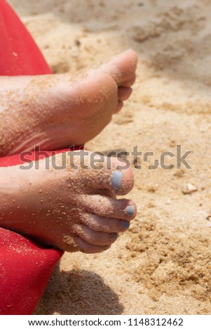 On the beach in the sand and on the red mattress, women's feet in the sun