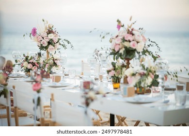 On the beach there are festive tables and chairs. Or a wedding table decorated with beautiful floral elements and candles? On the table were also glasses, plates, and cutlery. - Powered by Shutterstock