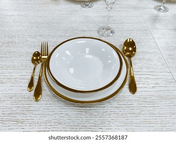 On a beautifully arranged table, there sits a pristine white plate accentuated with an elegant gold rim, accompanied by shiny silverware, creating an inviting and sophisticated dining atmosphere - Powered by Shutterstock