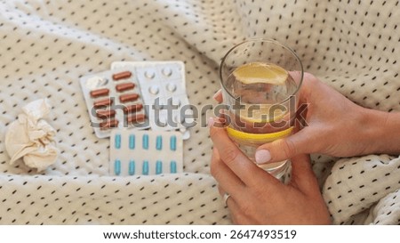 On the bed there are different types of medicines and tablets, a woman's hand holds a glass of water
