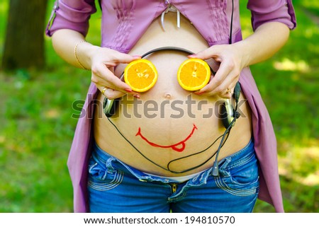 On the belly of a pregnant woman smiley face baby and headphones. The child listens to the music in the womb