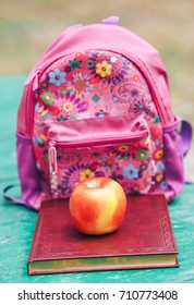 On the bench lie the book backpack and apple