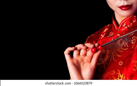on a black background can be seen part of the face of a Chinese girl with red lips and in a red traditional Chinese gown.