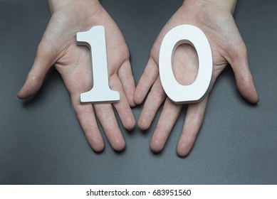 On a black background, female hand with number ten.