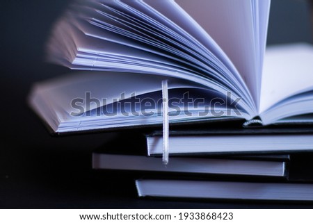 On a black background are a stack of books. On top of them lies an open book 