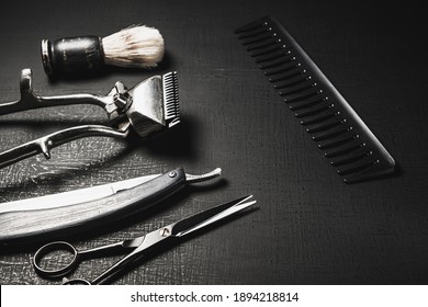 On a black surface are old barber tools. Vintage manual hair clipper comb razor shaving brush shaving brush hairdressing scissors. black monochrome. horizontal orientation. copy space