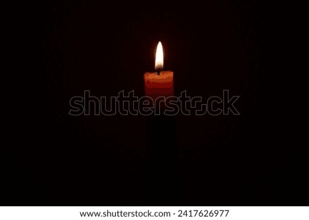 On a black textured background a burning red candle, , soft focus