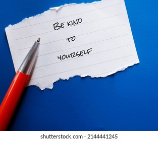 On blue background, handwritten text on note paper BE KIND TO YOURSELF, concept of self-kindness, be kind with understanding towards ourselves