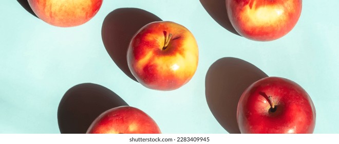 On a blue background lie red apples with yellow barrels. Bright sunlight falls on the apples creating a contrasting shadow.