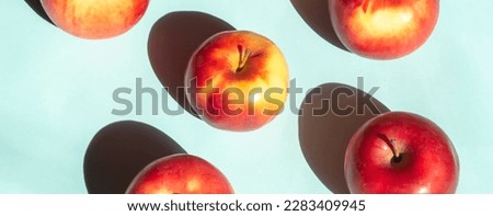 On a blue background lie red apples with yellow barrels. Bright sunlight falls on the apples creating a contrasting shadow.