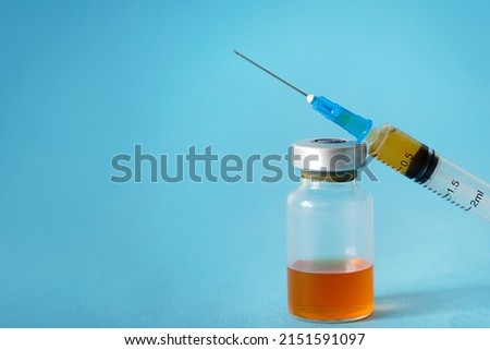 on a blue background a medical syringe with an orange medicine and a glass vial. concept of vaccination, subcutaneous injection, dose, treatment of diseases immunization, copy space, horizontal photo