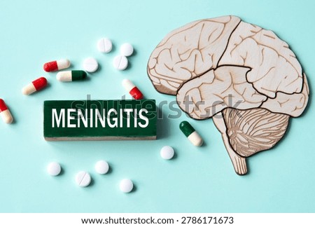 On a blue background with a model of a brain lies a wooden block with the words MENINGITIS