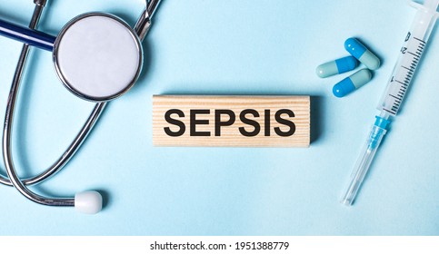 On a blue background, a stethoscope, a syringe and pills and a wooden block with the word SEPSIS. Medical concept