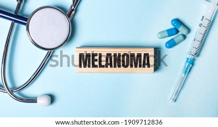 On a blue background, a stethoscope, a syringe and pills and a wooden block with the word MELANOMA. Medical concept
