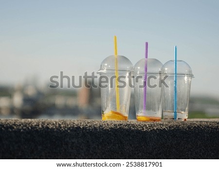 On a blue background, three empty transparent plastic cups with different straws stand. They symbolize the issue of environmental pollution, reminding us of the harm that plastic waste inflicts on the