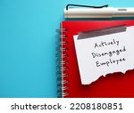 On blue copy space, torn paper on red notebook with handwritten text Actively Disengaged Employee - means unhappy employees who busy undermining workplace by getting others to share in discontent
