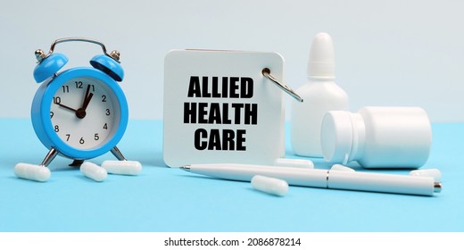 On A Blue Surface Lie Pills, An Alarm Clock And A Notebook With The Inscription - Allied Health Care