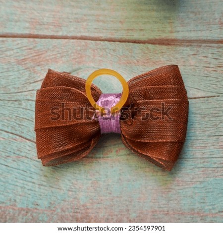 on a blue wooden table a brown bow is upside down with a pink ribbon in the middle with a silicone rubber band. view from above . hair accessories . bow