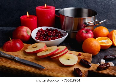 On a board are juicy apples, next to saucepan, plate with cranberries and burning candles.