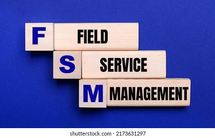 On A Bright Blue Background, Light Wooden Blocks And Cubes With The Text FSM Field Service Management