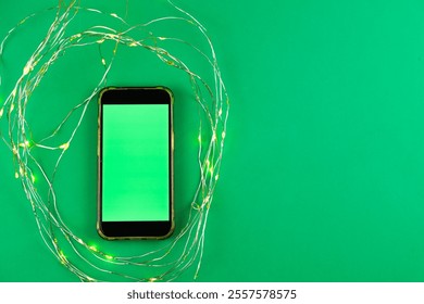 On a bright green background lies a phone with a green chroma key screen surrounded by a garland that glows yellow with space for text. High quality photo