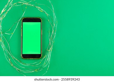 On a bright green background lies a phone with a green chroma key screen surrounded by a garland that glows yellow with space for text. High quality photo