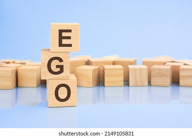 on a bright pale lilac and blue background, light wooden blocks and cubes with the text EGO. cubes is reflected from the surface.