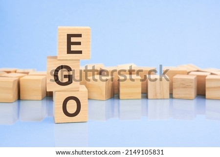 on a bright pale lilac and blue background, light wooden blocks and cubes with the text EGO. cubes is reflected from the surface.