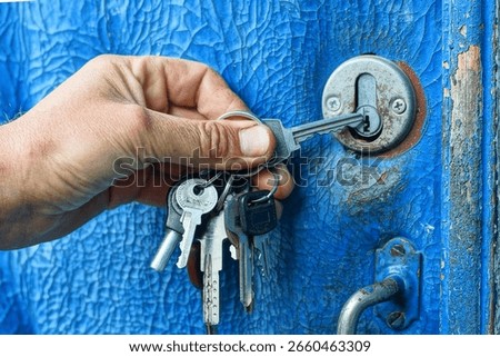 on a bunch of different keys, one iron gray key with a head and a blade in the hand of the men insert into the keyhole and open the old blue doors from the outside during the day