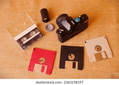 On a canvas background there are various audio cassettes from the 80s90s and floppy disks, CDs, analogue cameras and photographic rolls. View from above