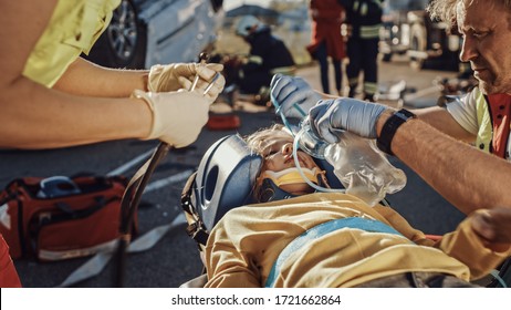 On the Car Crash Traffic Accident Scene: Paramedics Saving Life of a Traffic Accident Victim who is Lying on Stretchers. They Listen To a Heartbeat, Apply Oxygen Mask and Give First Aid Help - Powered by Shutterstock