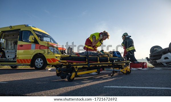 On the Car Crash Traffic Accident: Paramedics\
and Firefighters Rescue Injured Victims. Medics Give First Aid to a\
Little Girl on Stretchers.