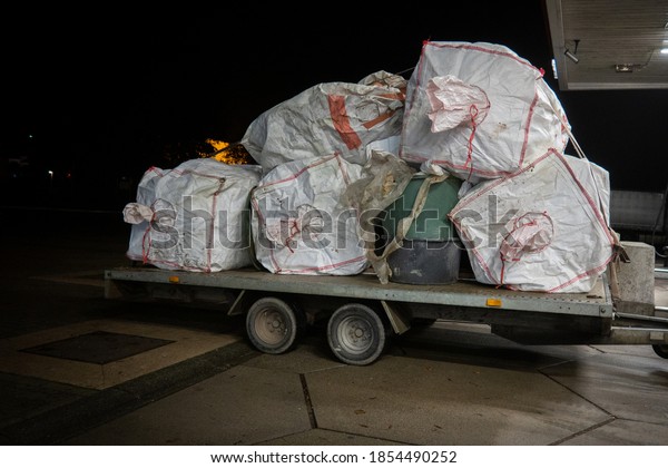 on a car trailer is a large load of white waste bags\
plastic garbage cans